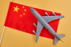 Aereo giocattolo grigio appoggiato su una bandiera cinese, su uno sfondo giallo.